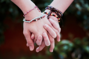 Foto, das die Hände zweier junger Menschen zeigt, die vor einem grünen Hintergrund ineinander verschlungen sind.